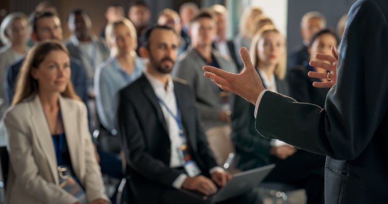 Ponente gesticulando sobre el escenario mientras el público escucha su ponencia