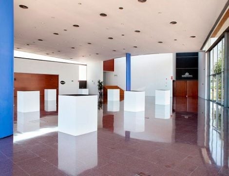 Modern art gallery interior with white display pedestals, polished red floor, recessed ceiling lights, and gallery walls in red and white