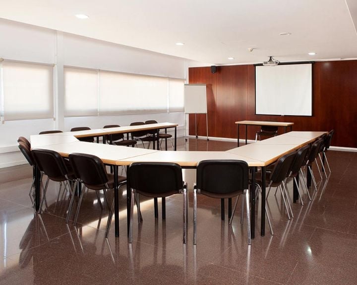 Modern conference room with U-shaped table, black chairs, projection screen, and burgundy accent wall